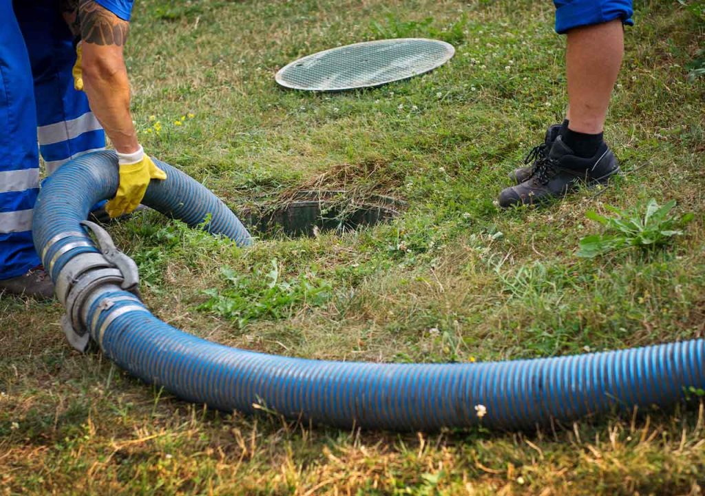 Septic tank maintenance with one being emptied by a large blue pipe.