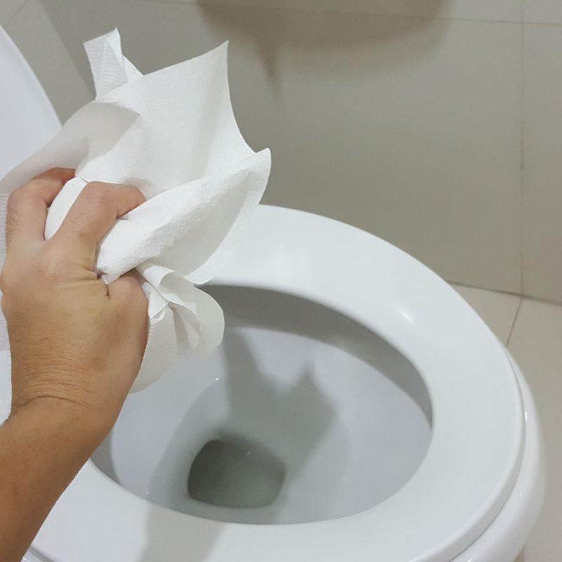 Throwing tissues down a white toilet.