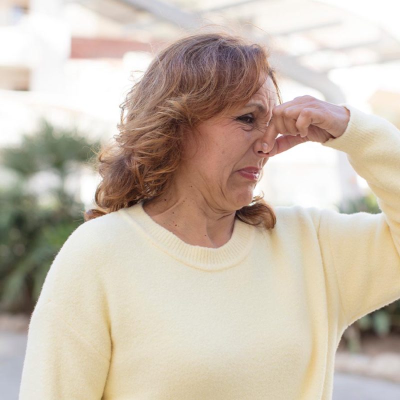 A woman in a white jumper is holding her nose at a bad smell.