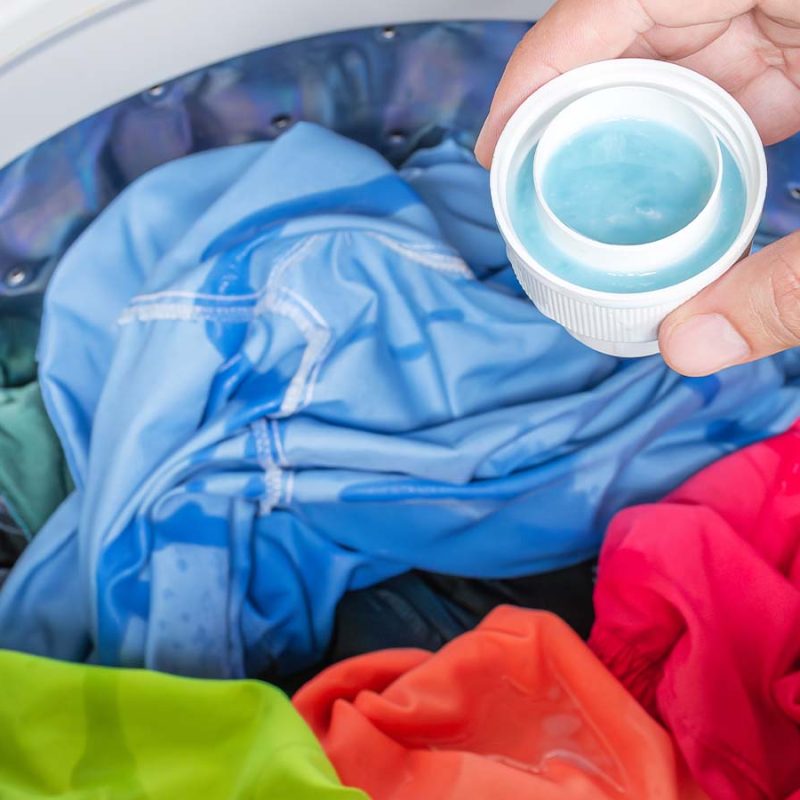 A person about to add liquid laundry detergent to a washing machine of coloured clothes.