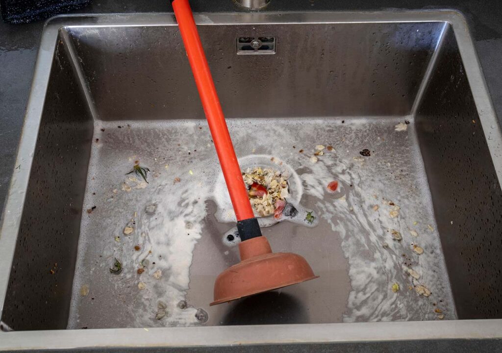 A blocked kitchen sink with a plunger.